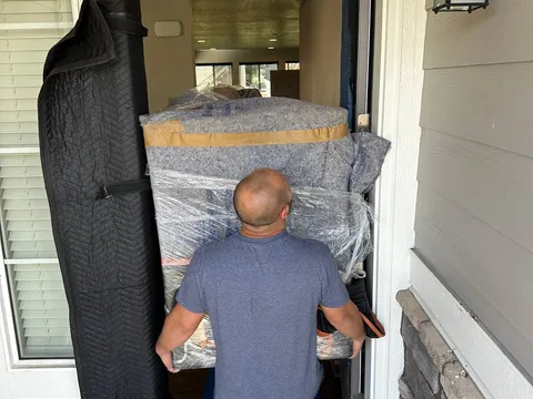 A Sun City Moving crew member carrying wrapped furniture through a front door