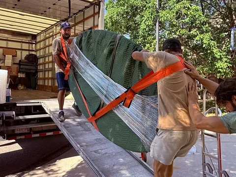 Sun City Moving crew members carrying a wrapped item down a truck ramp