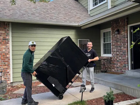 Two Sun City Moving crew members carrying a wrapped television outside a home