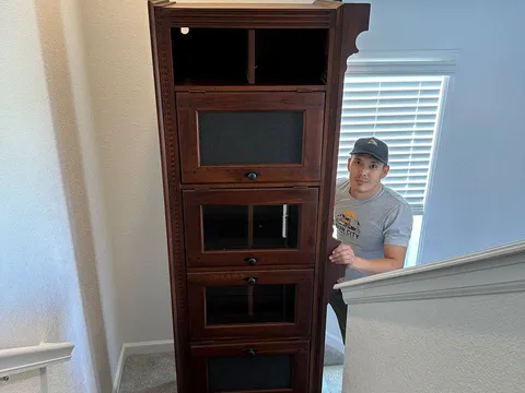 A Sun City Moving crew member carrying a wooden cabinet down a staircase