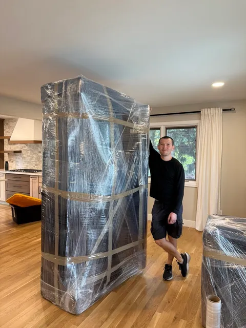 A Sun City Moving crew member next to a tall piece of furniture fully wrapped in plastic and tape