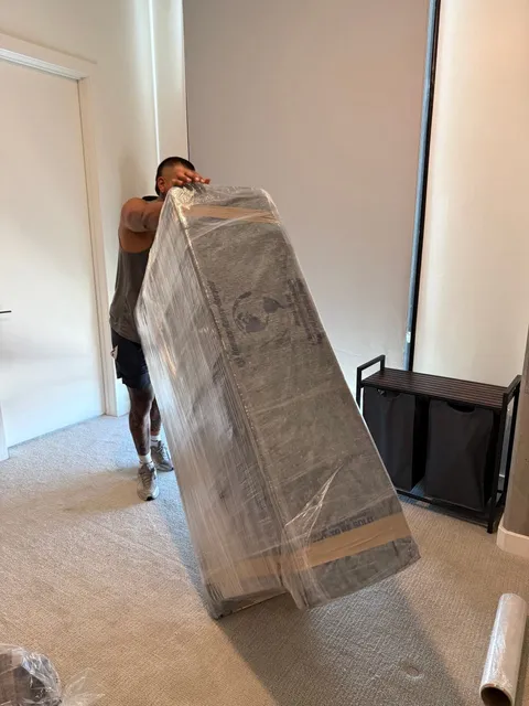A Sun City Moving crew member tilting a large wrapped item onto its edge to move it