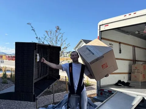 A Sun City Moving crew member carrying a box while helping unload a customer's rental truck