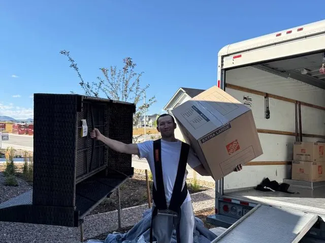 A Sun City Moving crew member carrying a box while helping unload a customer's rental truck